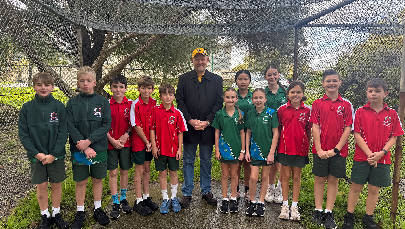 A group of primary school student, in uniforms stand in the cricket nets with an adult.